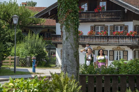 Paar in Tracht mit Kleinkind und altem Bauernhaus im Hintergrund
